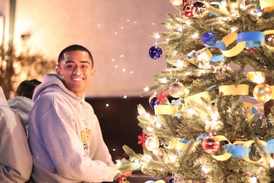 Fano Maui from the Oil Tech program sits next to the Christmas tree and smiles for the camera. 